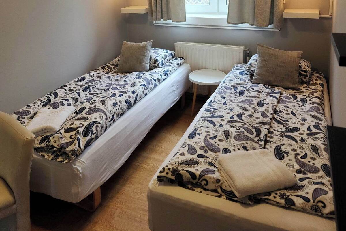 A small, cozy room with two single beds, a small table, and a chair.