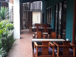 An outdoor seating area with wooden tables and chairs, a brick pathway, and green plants.