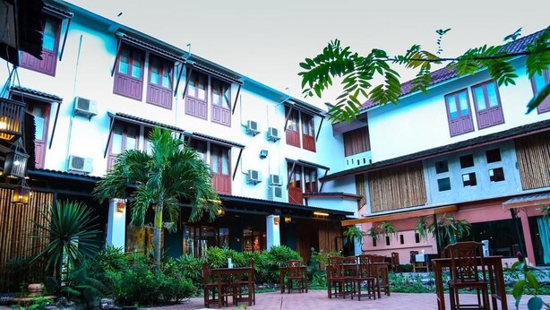 A courtyard with traditional architecture, multiple dining areas, and lush greenery. - Charming Lao Hotel (Oudomxay)