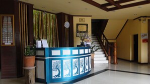 A reception desk with a clock, framed certificates, and a staircase in the background. - Charming Lao Hotel (Oudomxay)
