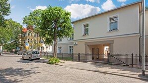 Edifici amb entrada enjardinada, carril d'accés reixat i un cotxe estacionat.