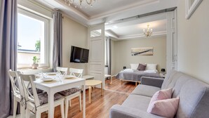 Habitació d'hotel moderna amb zona de menjador, un sofà, un llit i una televisió.