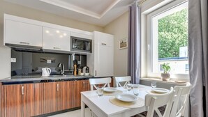Una cuina moderna amb una illa central, armaris blancs i una zona de dinar amb taula preparada per a quatre.