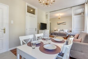 Habitación compacta y bien iluminada con una mesa de comedor preparada para cuatro personas, un sofá, una cama y un televisor.
