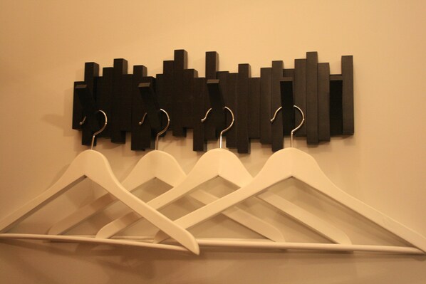 A wall-mounted coat rack with multiple white hangers and a black abstract art piece above it. - Guesthouse Vellir (Skeidflotur)