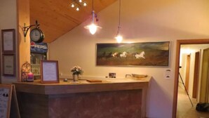 Un área de recepción con mostrador de mármol, un reloj, un letrero de Pepsi, un certificado enmarcado y una pintura de caballos.