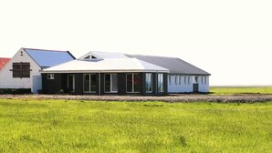 Una casa moderna con un amplio ventanal y un panel solar en el techo, rodeada de un campo verde.