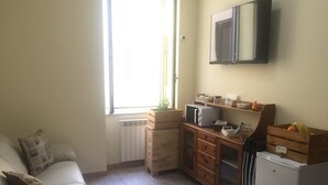 A compact kitchen with a built-in microwave, a small refrigerator, wooden cabinets, and a window providing natural light. - Naples to live (Naples)