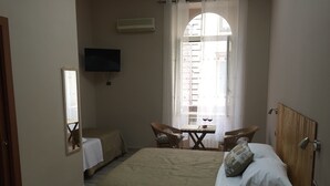 A bedroom with a bed, two chairs, a small table with wine glasses, a TV, and a window with curtains. - Naples to live (Naples)