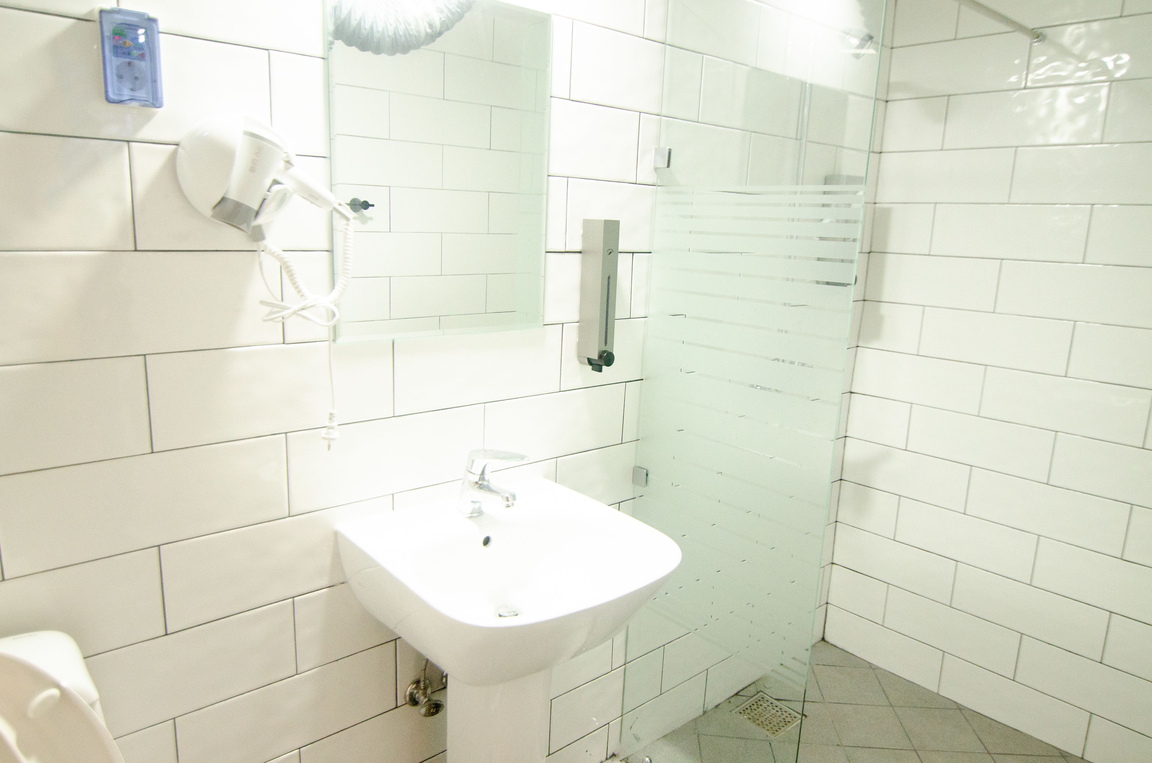 A bathroom with white tiles, a sink, a hairdryer, and a mirror.