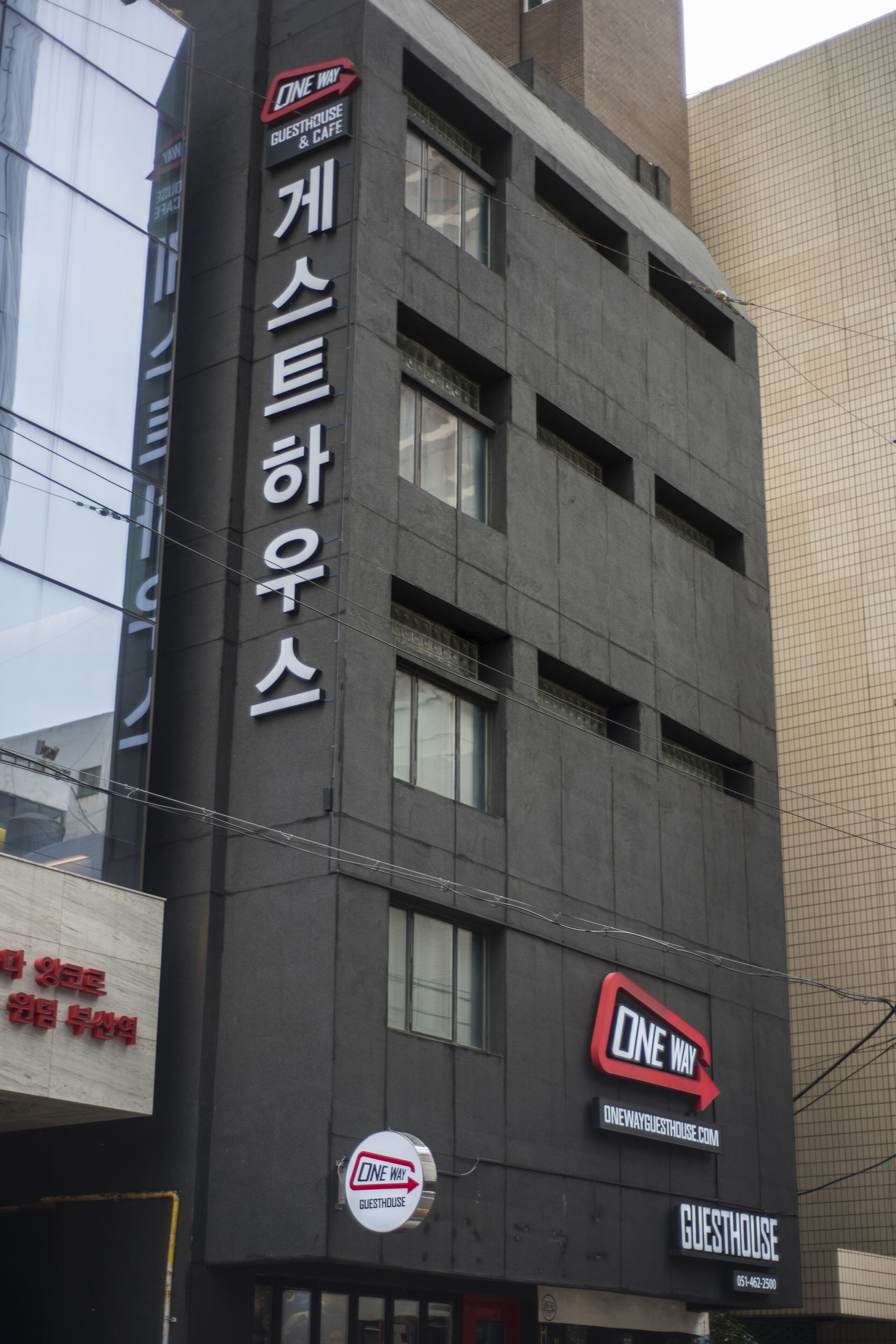 Un edificio con un letrero que dice 'ONE WAY GUESTHOUSE', con un diseño moderno, múltiples ventanas y fachada oscura.
