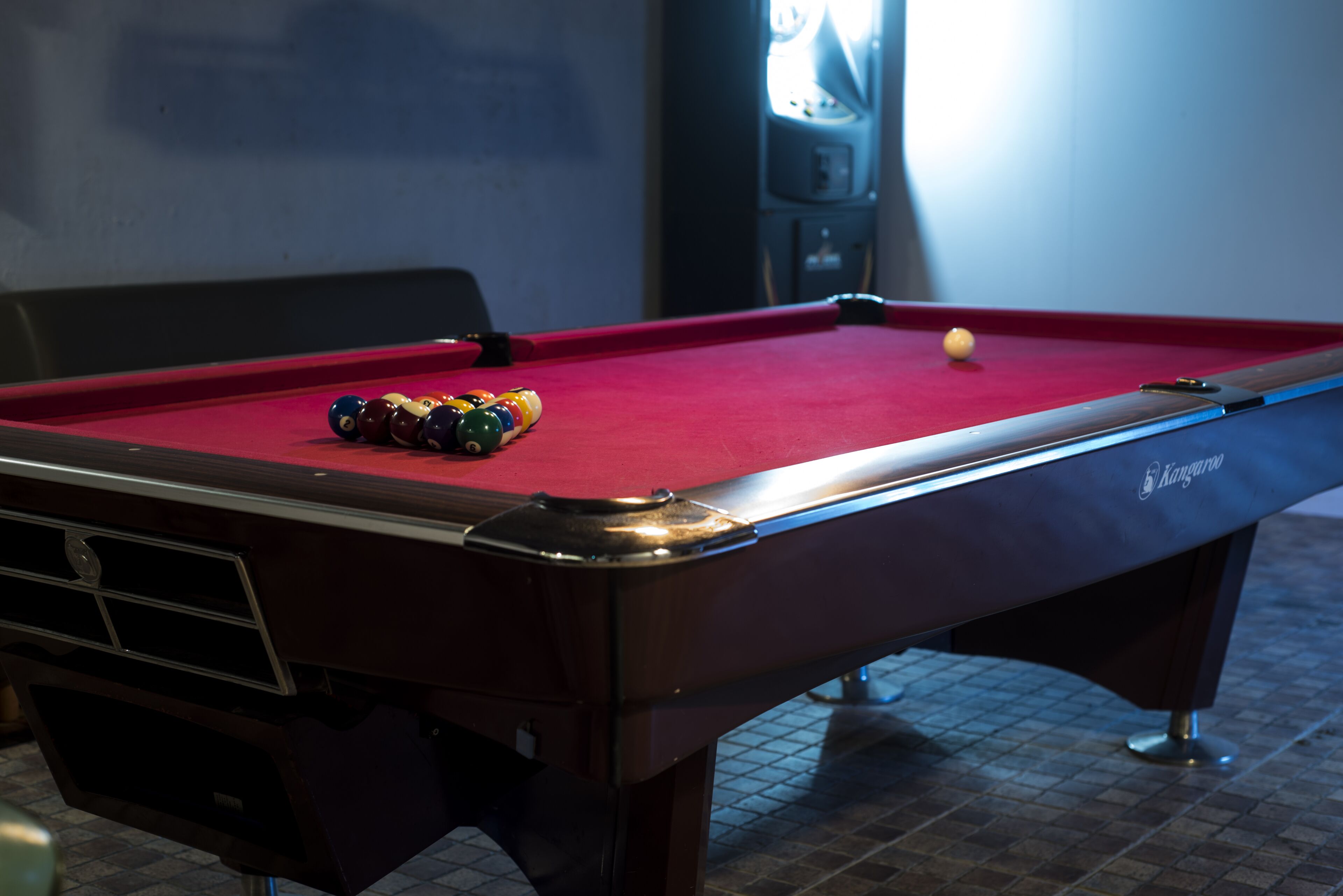 A pool table with a red felt surface, a cue ball, and a set of colored balls.