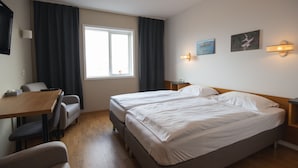 Une chambre d’hôtel avec un lit double, un bureau avec une chaise, une télévision et une fenêtre avec des rideaux.