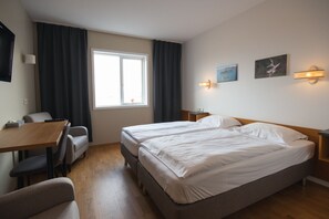 A hotel room with a double bed, a desk with a chair, a television, and a window with curtains. - Hótel Búrfell (Vik I Myrdal)