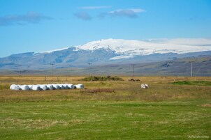 A rural landscape with hay bales, a tractor, and a snow-capped mountain in the background.