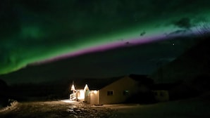 Une maison avec un porche illuminé, sous une aurore boréale verdoyante.