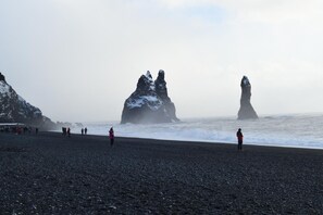 A rocky beach with large rock formations and people walking along the shore. - Hótel Búrfell (Vik I Myrdal)