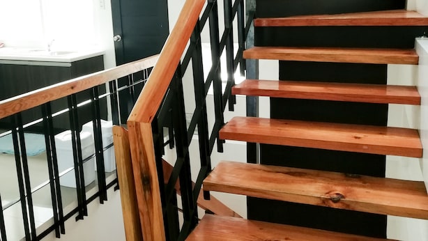 A wooden staircase with black railings, a white wall, and a wreath on the wall. - 87 Guesthouse (Baguio)