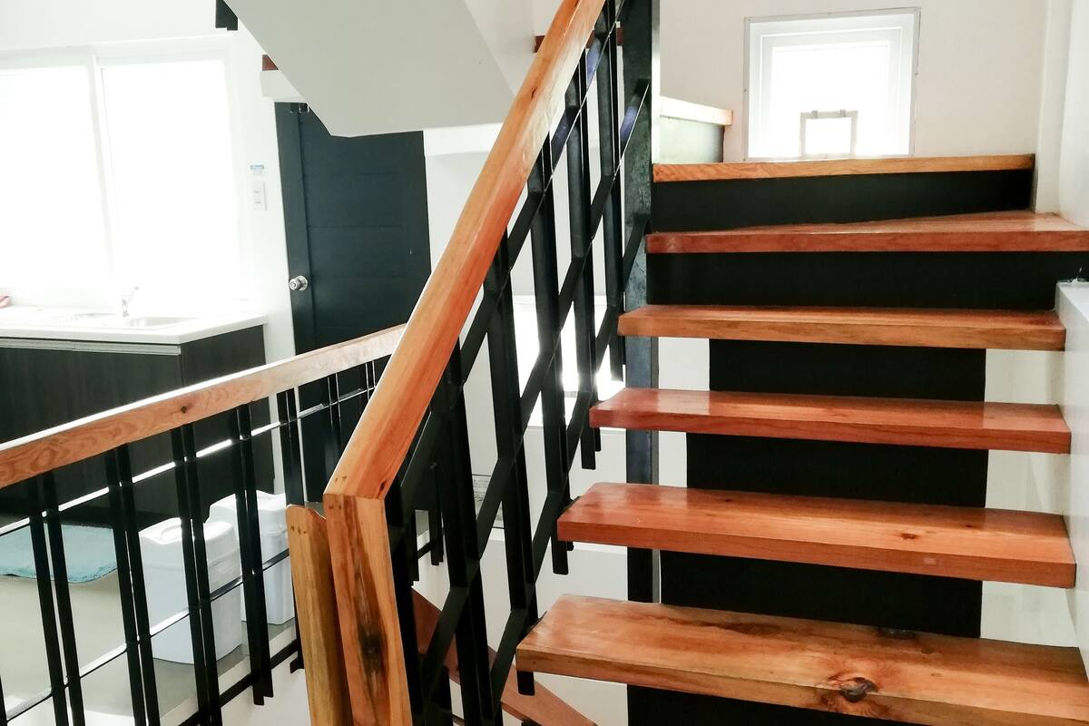 A wooden staircase with black railings, a white wall, and a wreath on the wall.