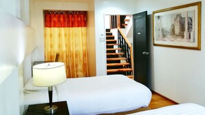 A hotel room with two beds, a nightstand with a lamp, a staircase, and a framed picture on the wall. - 87 Guesthouse (Baguio)