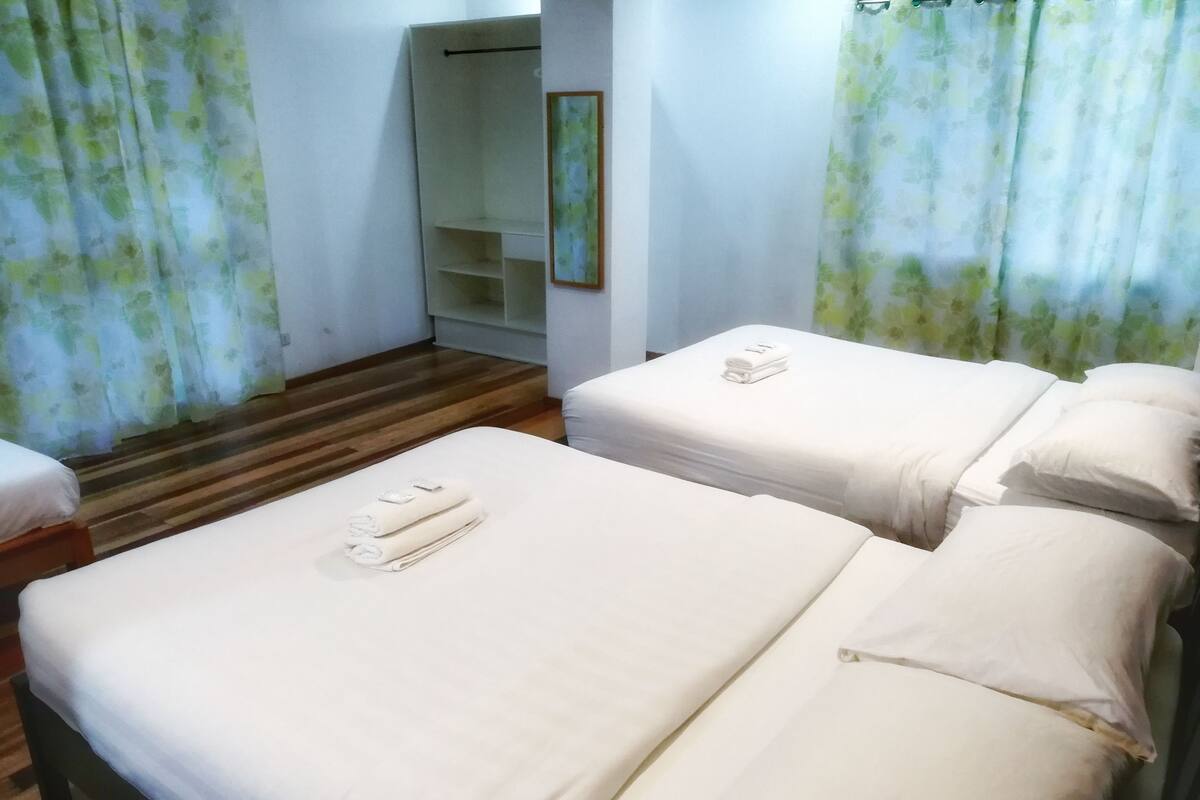 A hotel room with two beds, a wooden floor, and floral curtains.