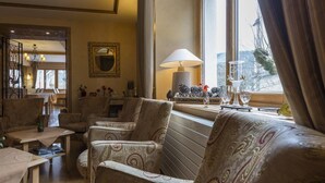 A cozy living room with patterned sofas, a table with books, and a window with a view. - La Couronne (Jougne)