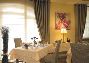 A dining area with a table set for two, a lamp, and a painting on the wall.