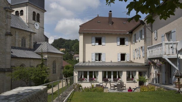 A two-story building with a balcony, a clock tower, and a garden area with outdoor seating. - La Couronne (Jougne)