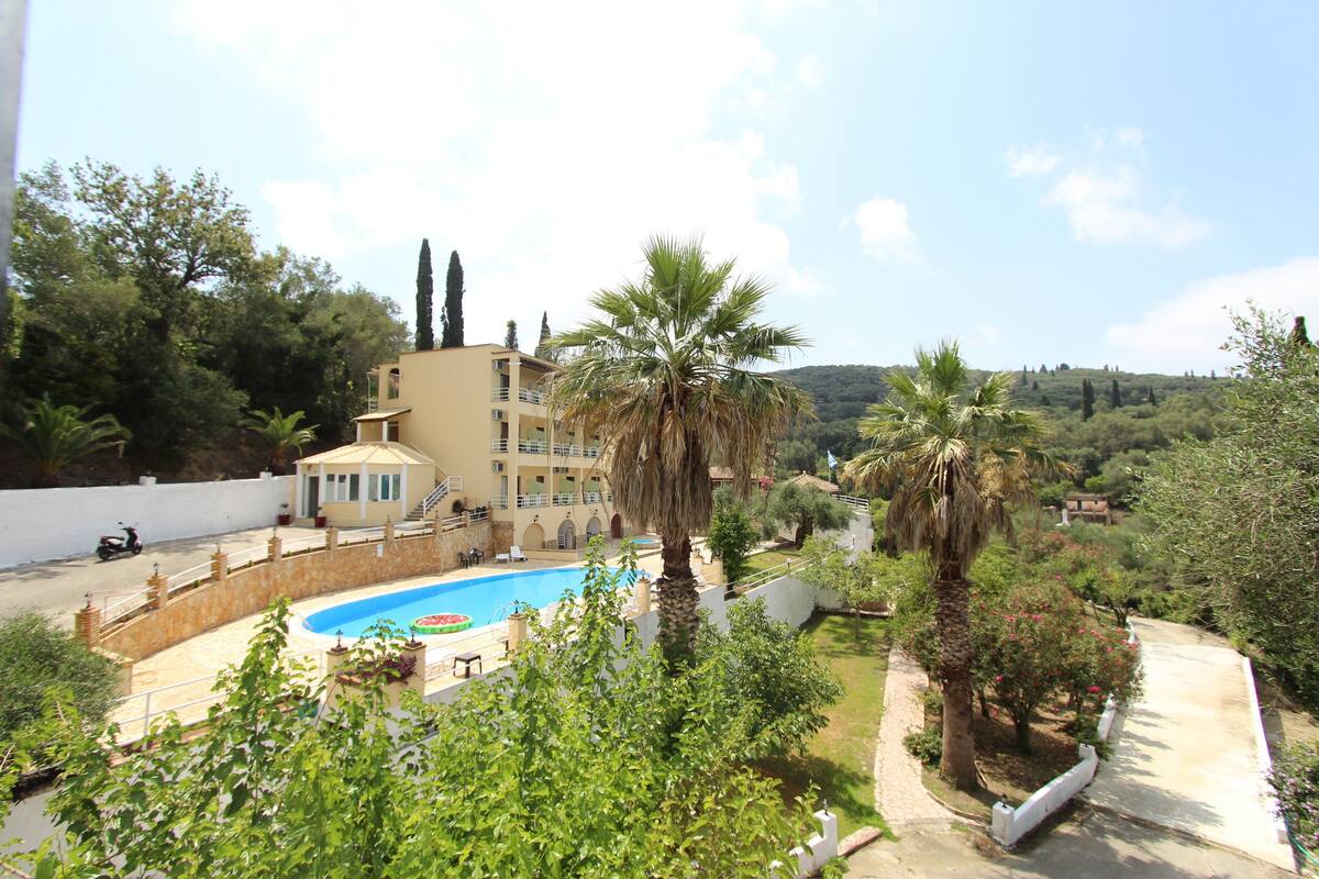 A pool surrounded by a garden with palm trees and a building with multiple balconies.