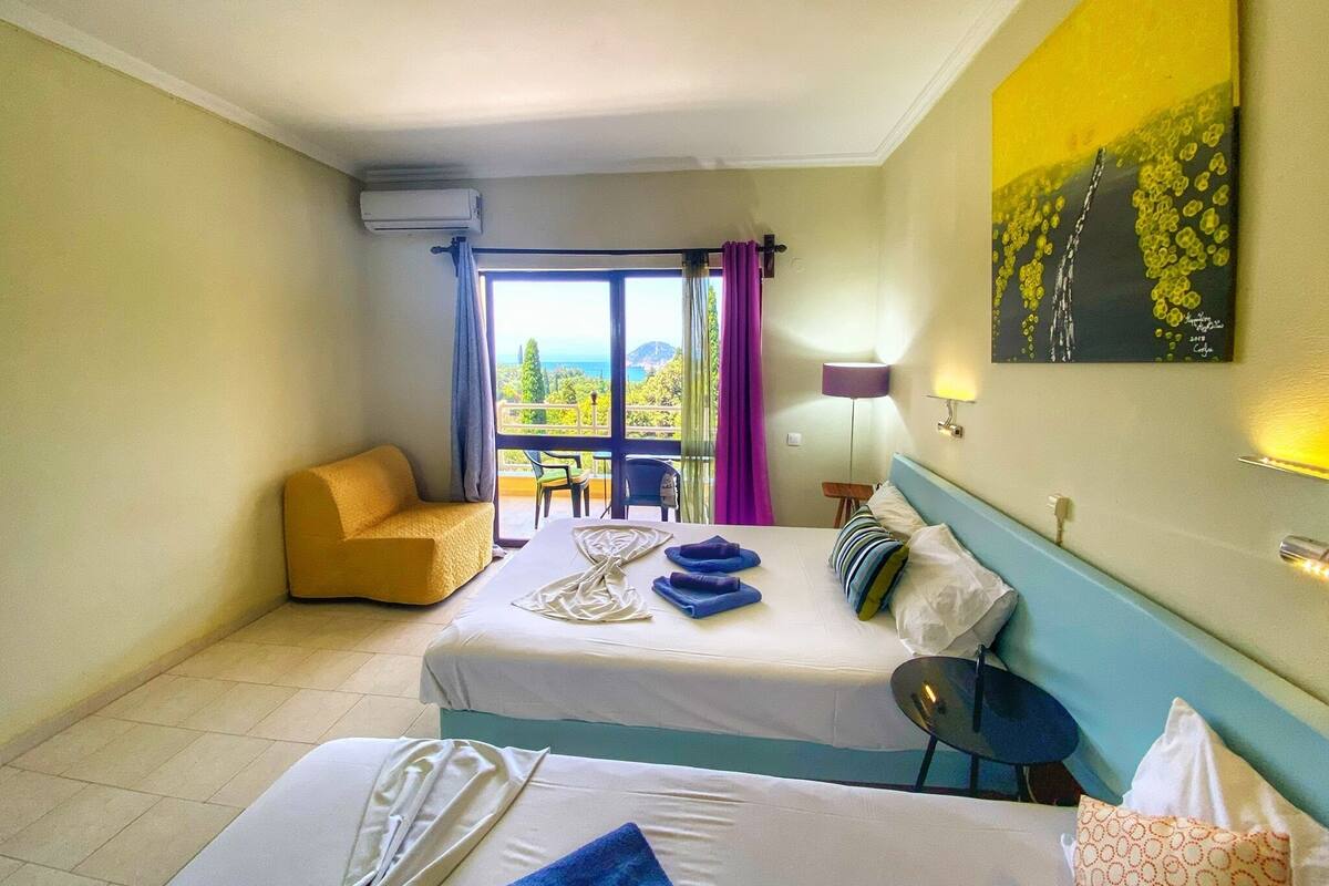 A hotel room with two beds, a sofa, a table, and a view of the outdoors.