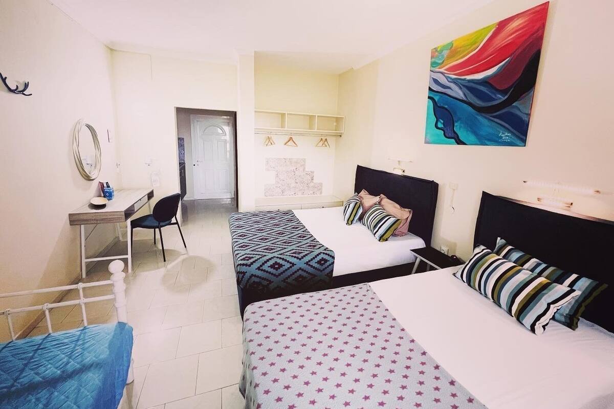 A room with two beds, a desk, a chair, a mirror, and a painting on the wall.