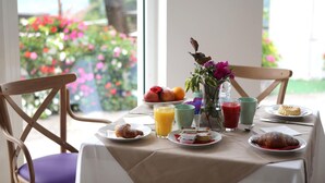 A breakfast table with croissants, pastries, and fruit, set against a window with a view of flowers and greenery. - Hotel Corona (Caprino Veronese)