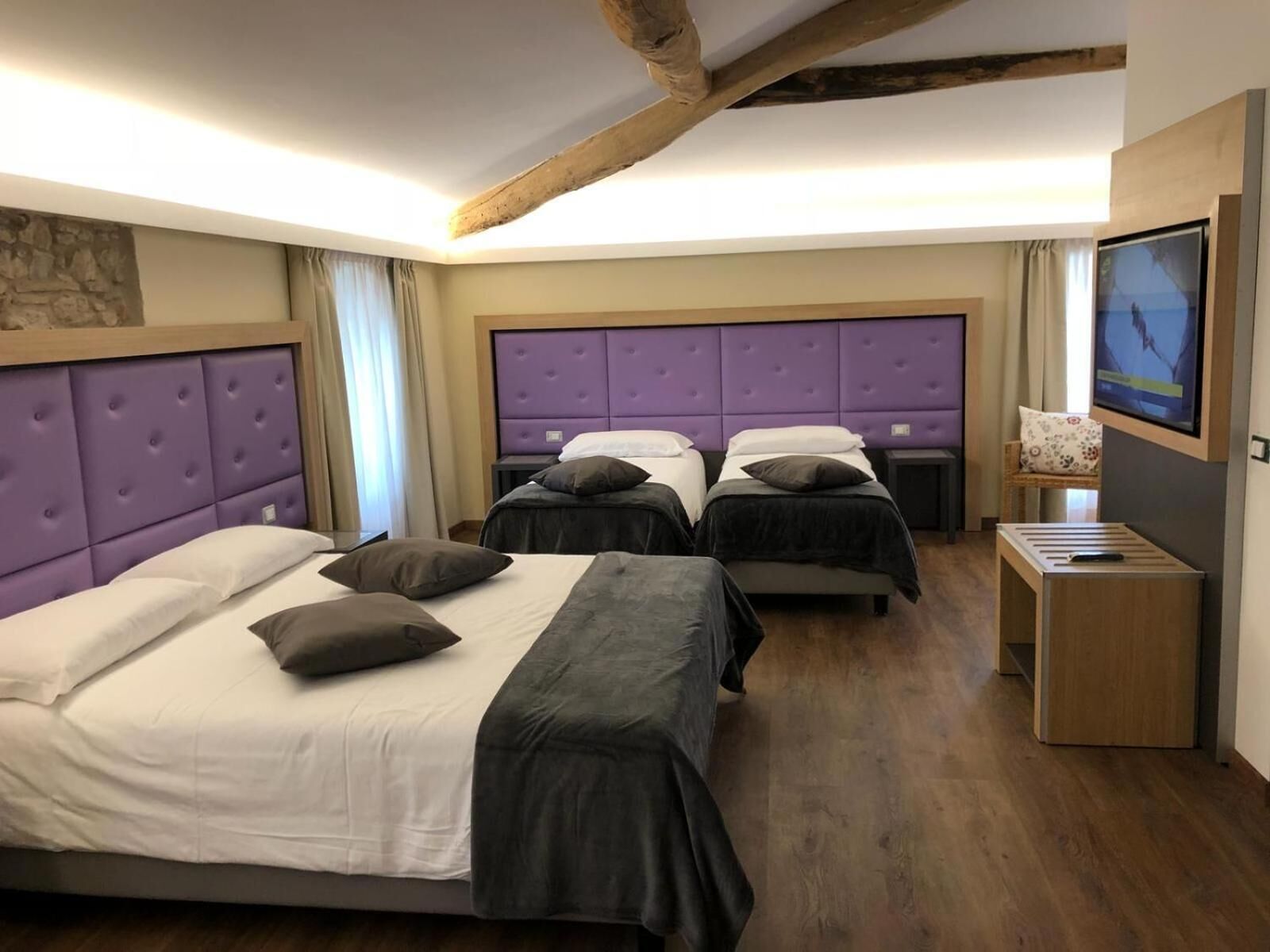 Habitación de hotel con dos camas, televisión y una viga de madera en el techo.