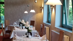 A dining area with tables set for a meal, featuring white tablecloths, glassware, and floral centerpieces. - Weinhotel Atrium (Bad Salzuflen)