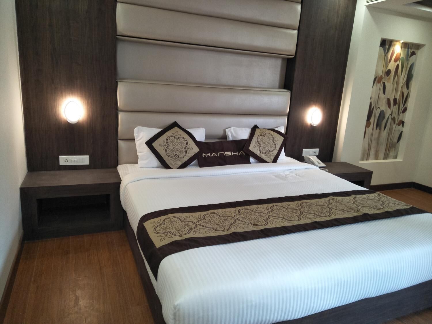 Una habitación de hotel moderna con una cama grande, cabecera con iluminación integrada, mesita de noche y teléfono de pared.