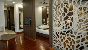 A modern hotel room with a wooden floor, a bed, a TV, and a decorative white partition. - Hotel Mansha Regency (Port Blair)