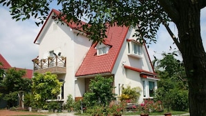 A two-story house with a red roof, a balcony with plants, and a well-maintained garden. - Yishingarden B&B (Shoufeng)