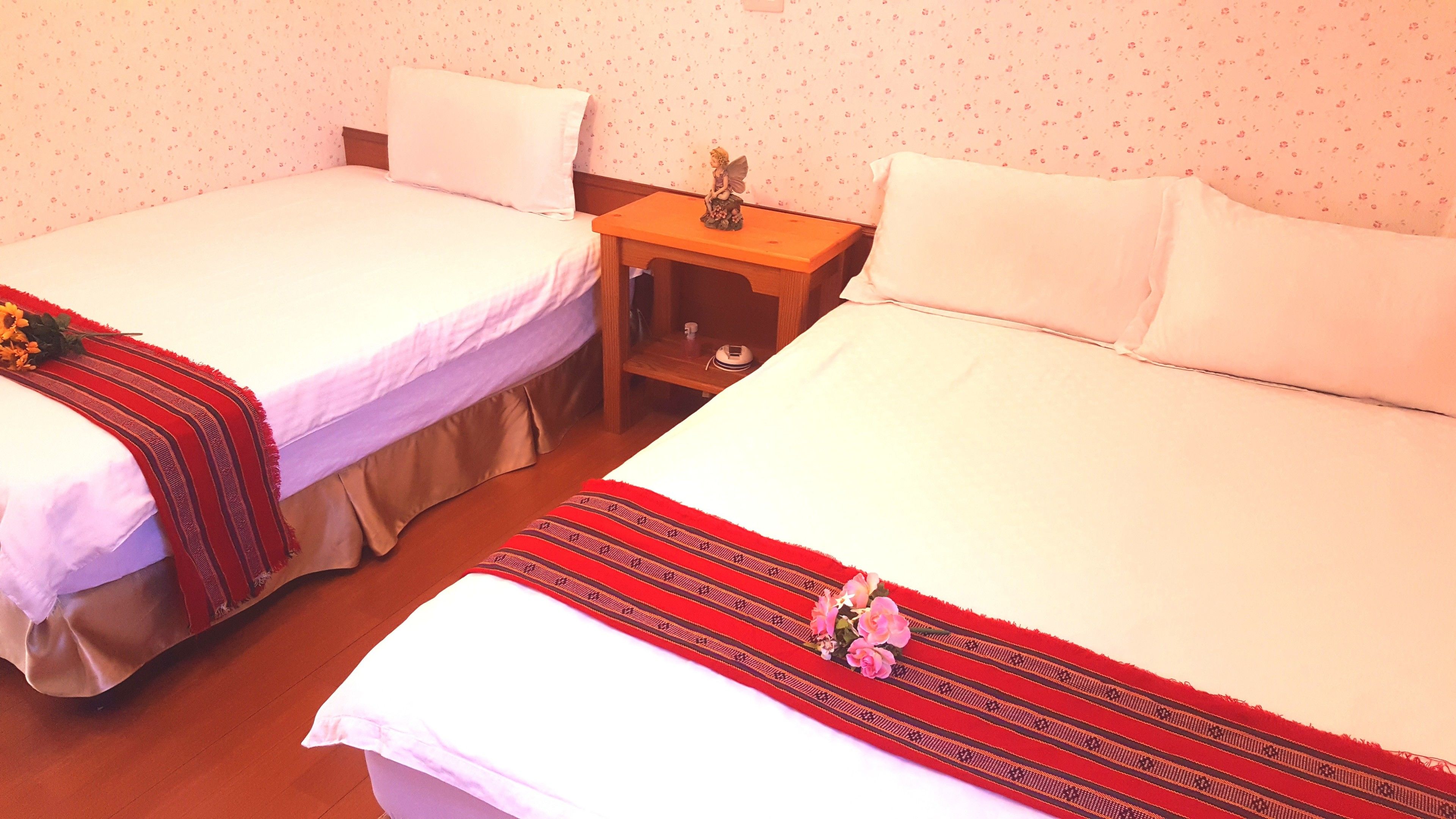 Two single beds with white linens, a nightstand with a small figurine, and a floral-patterned wall.