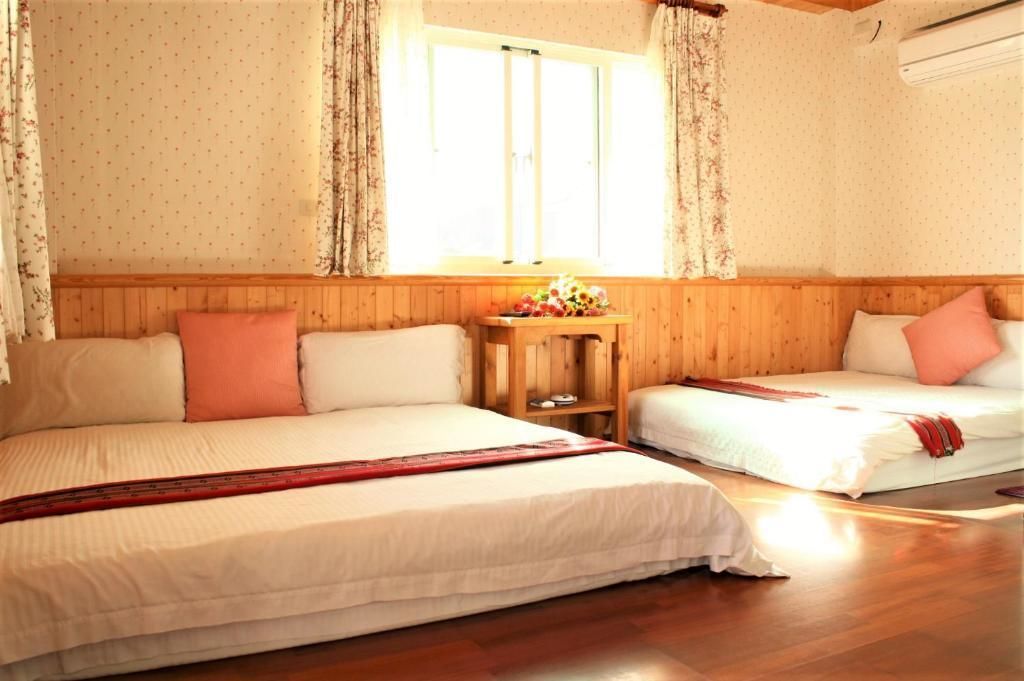 A room with two beds, wooden paneling, a small table with a vase of flowers, and a window with curtains.