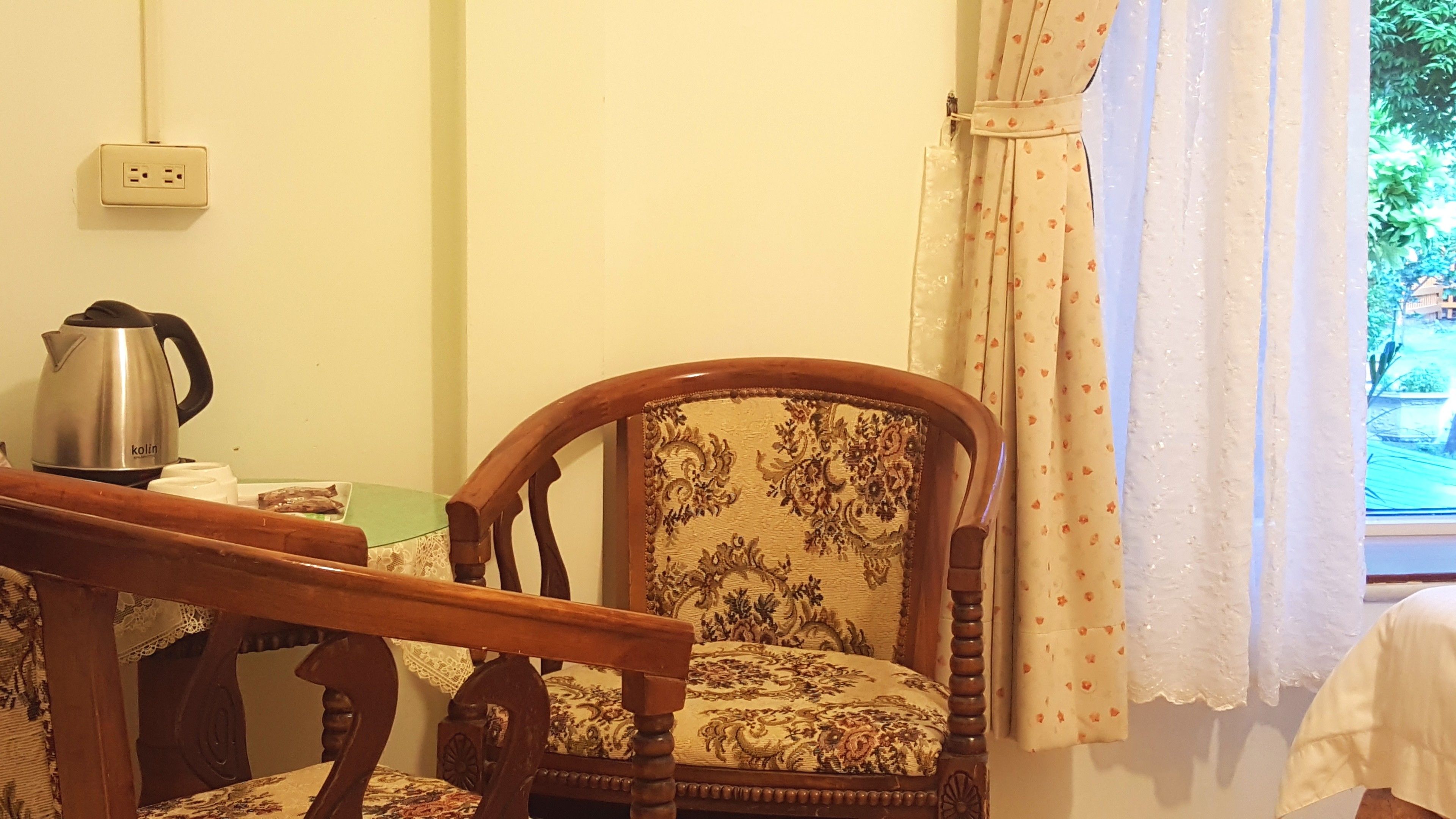 A wooden chair with a floral pattern, a kettle, and a power outlet on the wall.