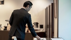 A man in a dark suit standing at a desk in a modern office setting with a chair and a whiteboard in the background. - Kyoto Yamashina Hotel Sanraku (Kyoto)