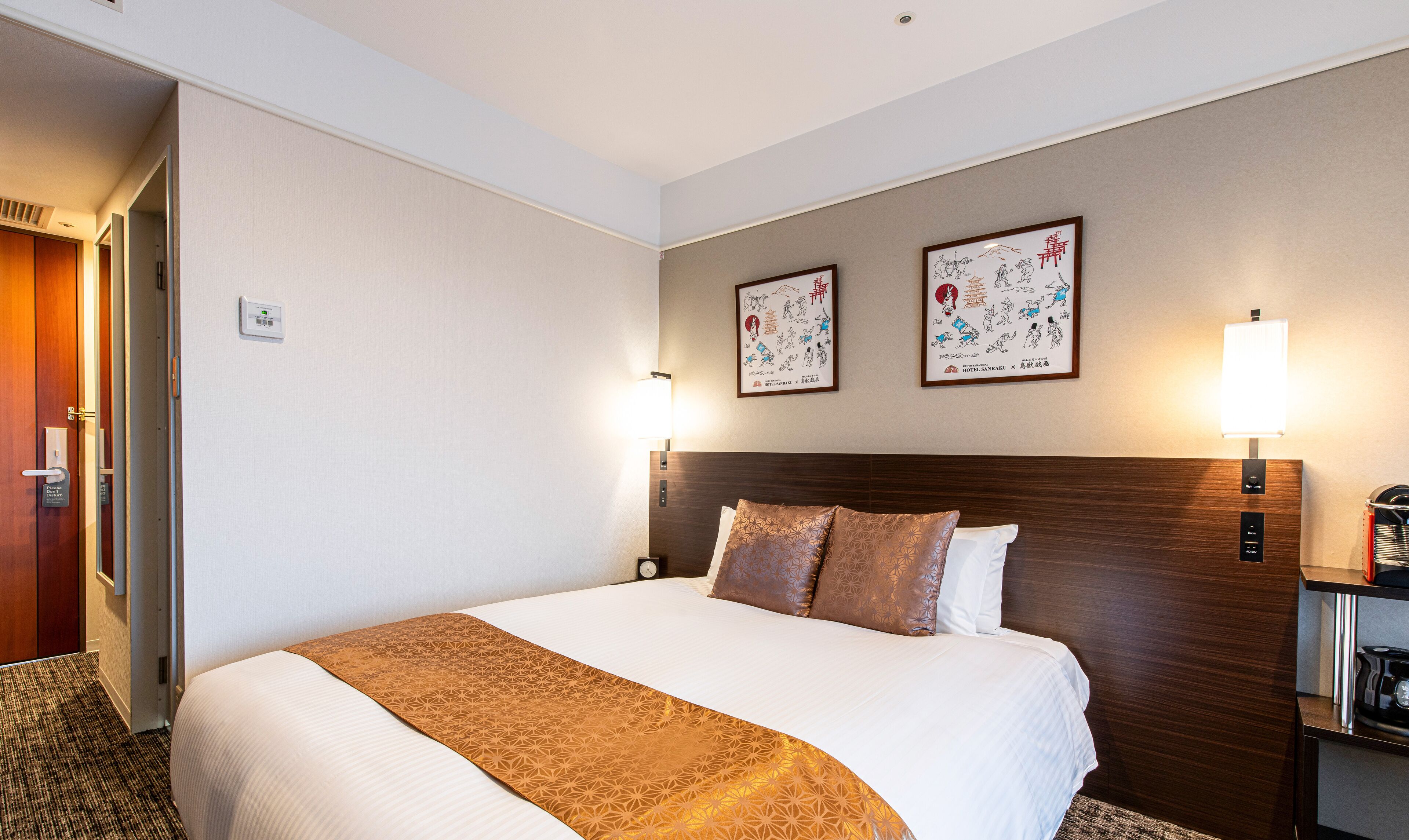 Ein Hotelzimmer mit einem großen Bett, einem Holzkopfstück, zwei Wandlampen und einem gerahmten Bild an der Wand.