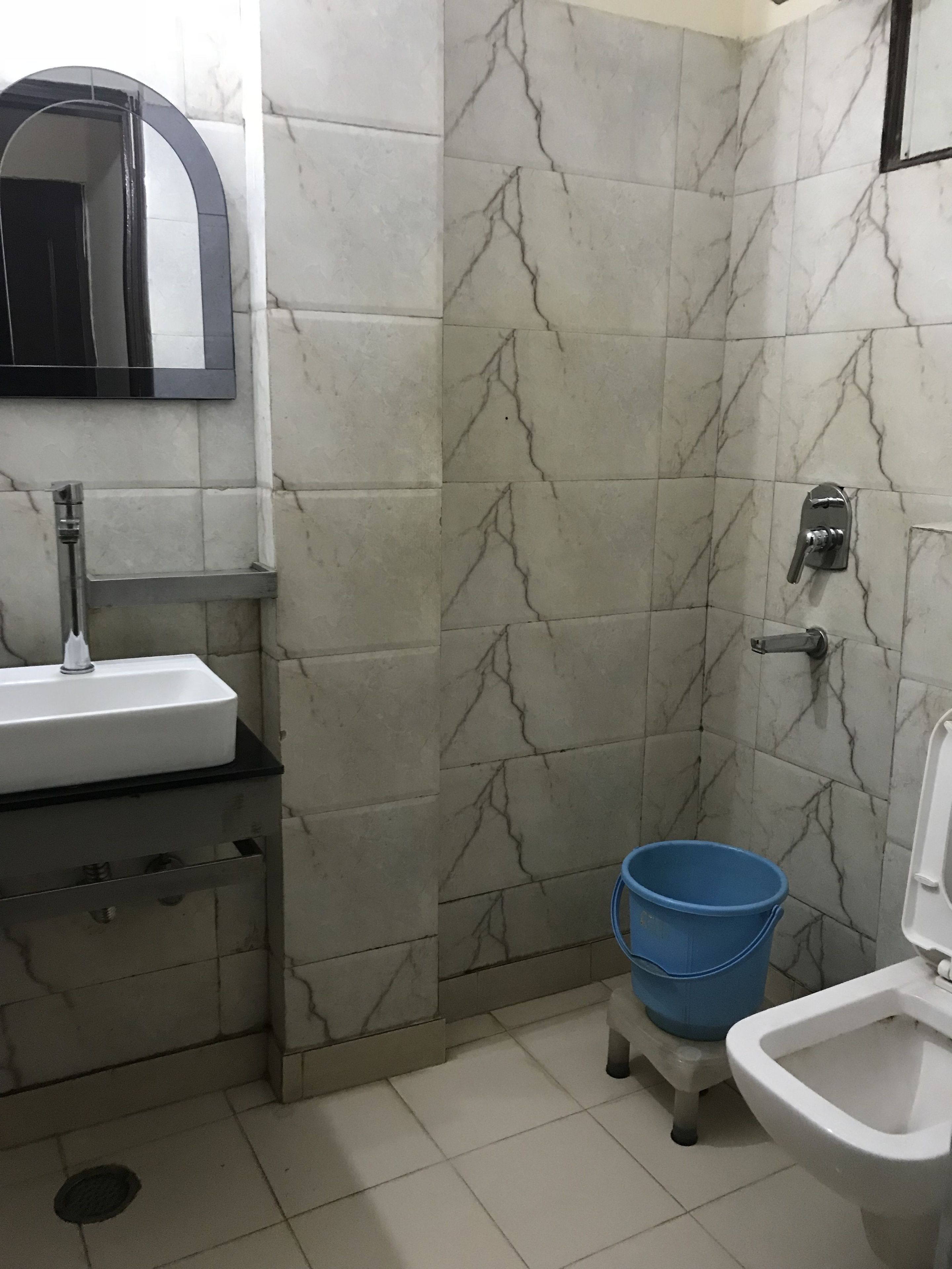 A bathroom with a sink, mirror, toilet, and blue bucket.