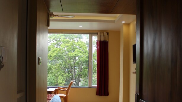 A hallway leading to a room with a bed, a window with curtains, and a door. - White Coral (Port Blair)
