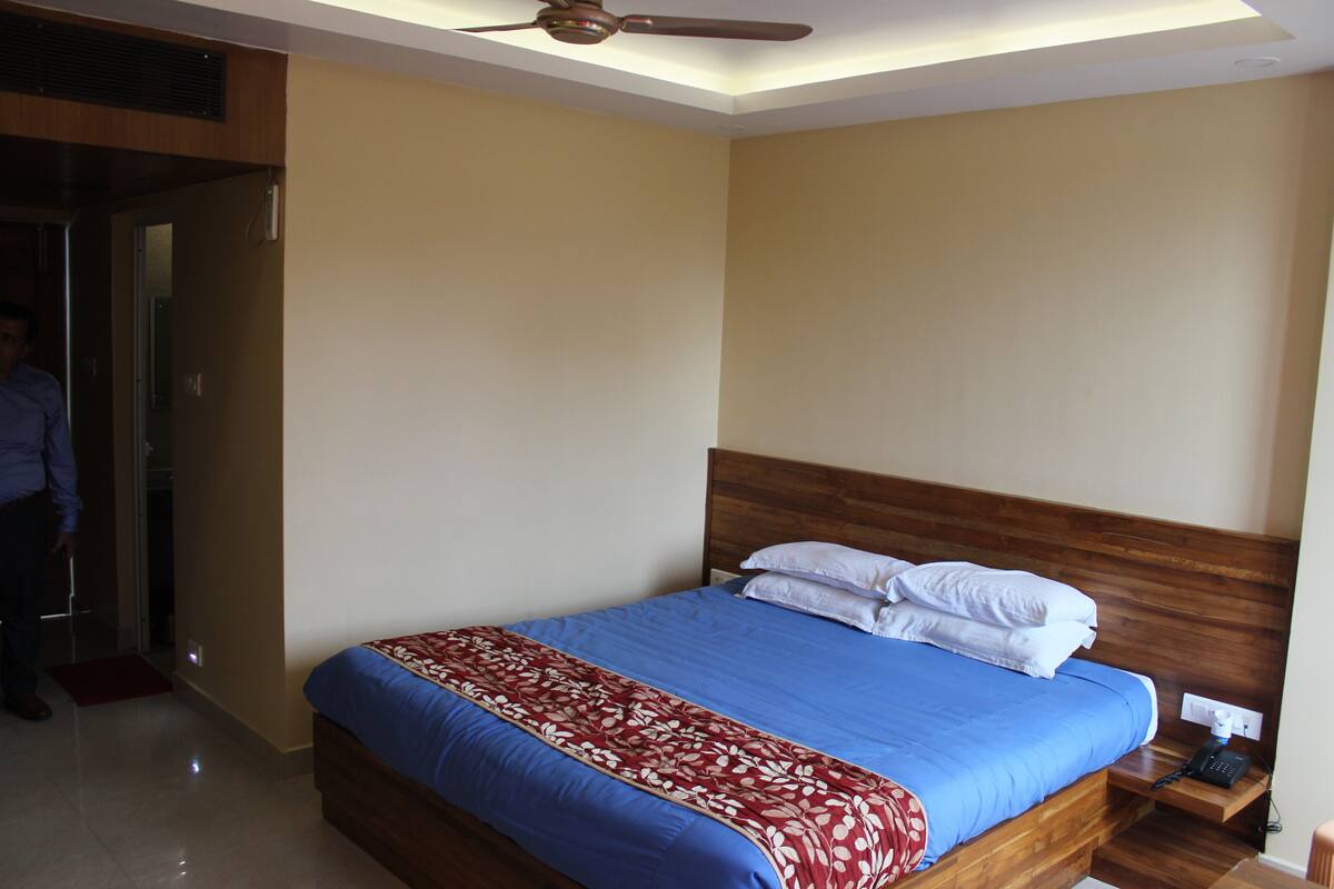 Una cama bien hecha con una colcha azul y roja, un cabecero de madera y una mesita de noche con un teléfono.