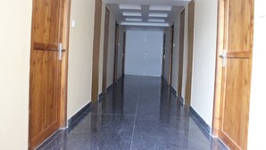 A hallway with wooden doors on either side, a tiled floor, and a ceiling with recessed lighting. - White Coral (Port Blair)