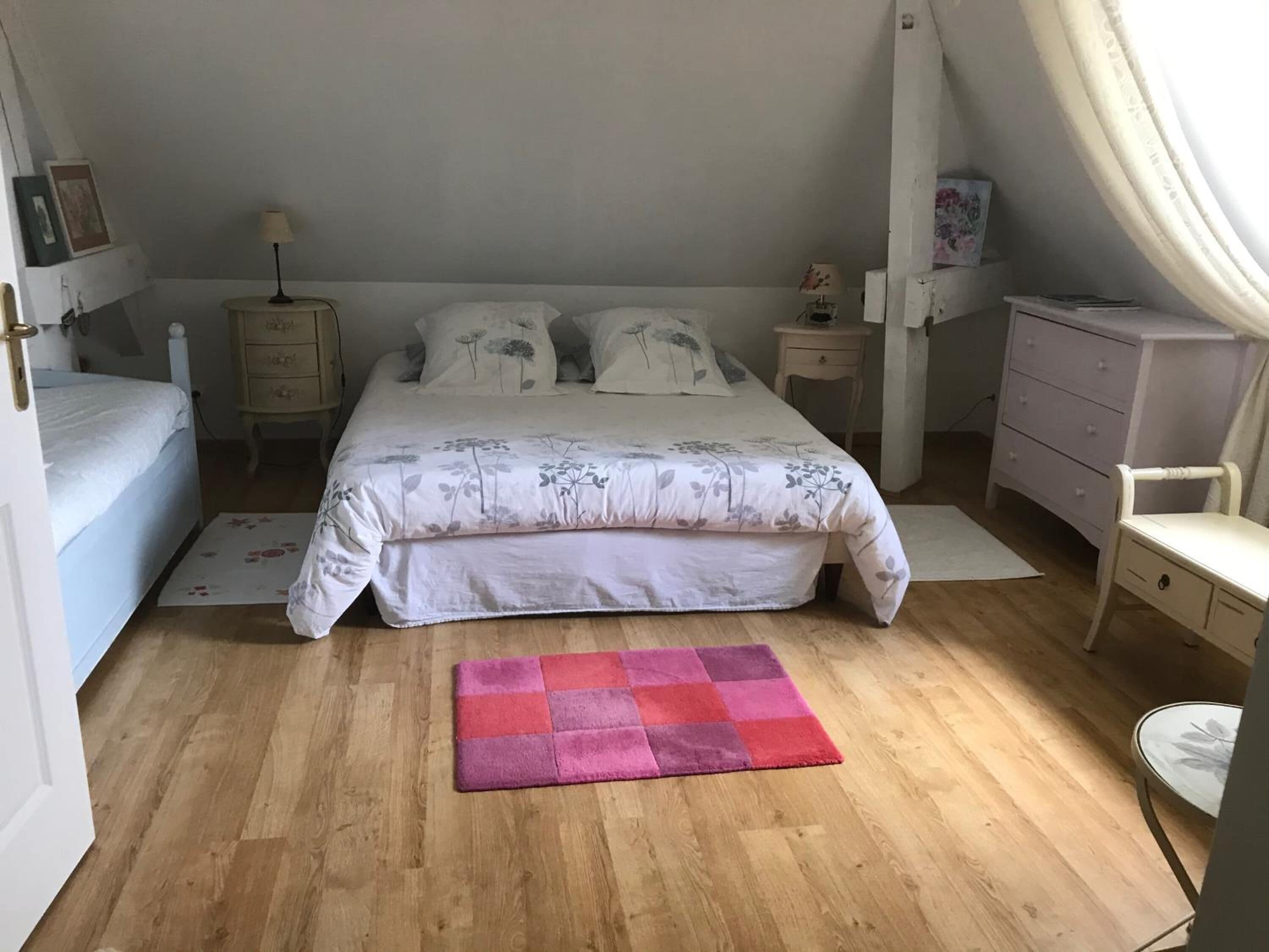 Un dormitorio con cama, mesitas de noche, una silla, cómoda y ventana con cortinas.