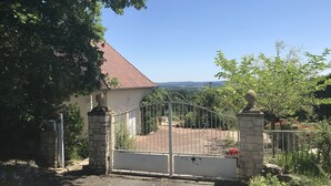 A gated entrance to a property with a stone wall and metal gate, surrounded by greenery and a clear sky. - La Maison Du Parc (Saint-Raphaël)