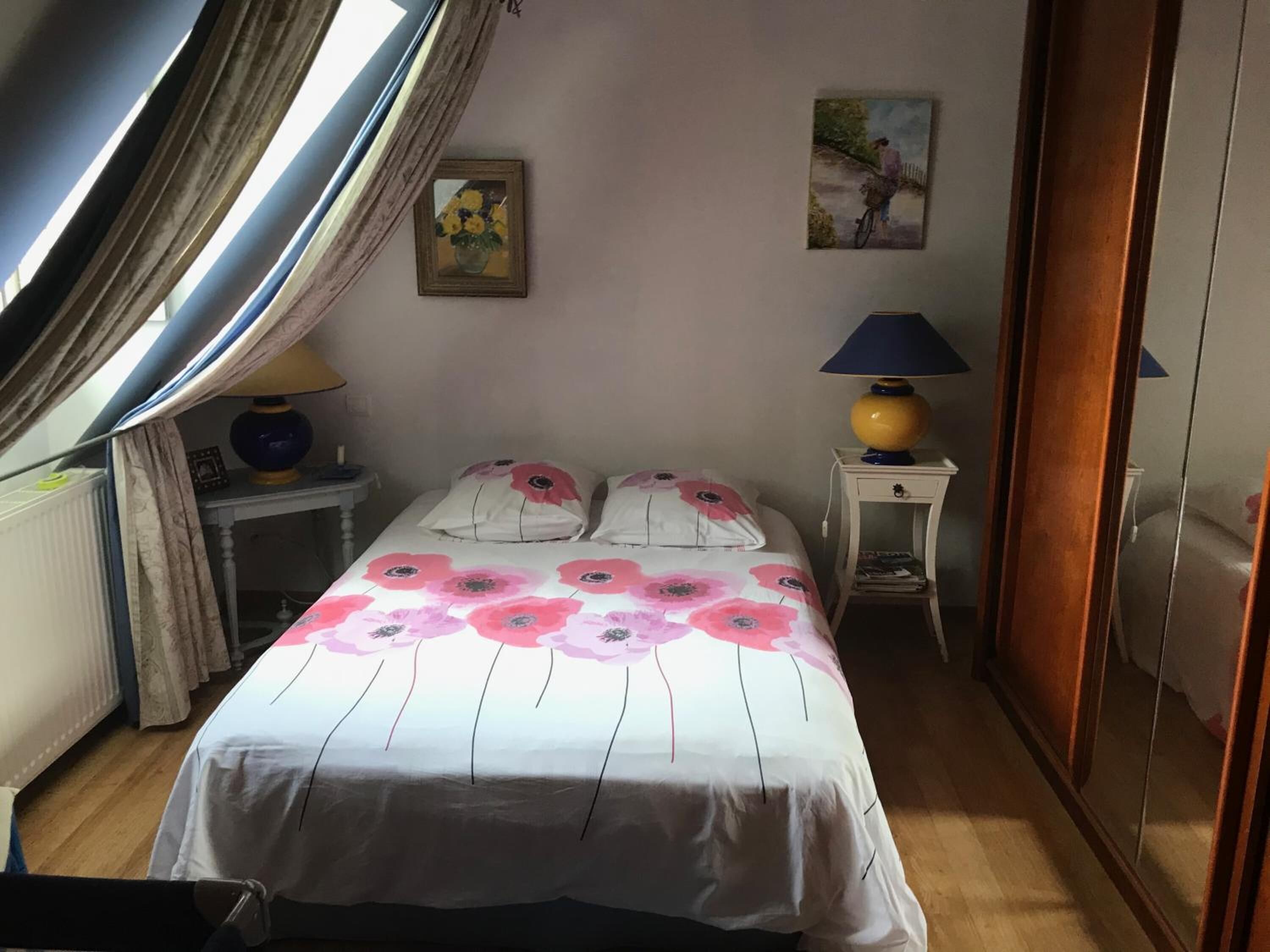 A bedroom with a bed, two bedside tables, a lamp, a painting, and a wardrobe.