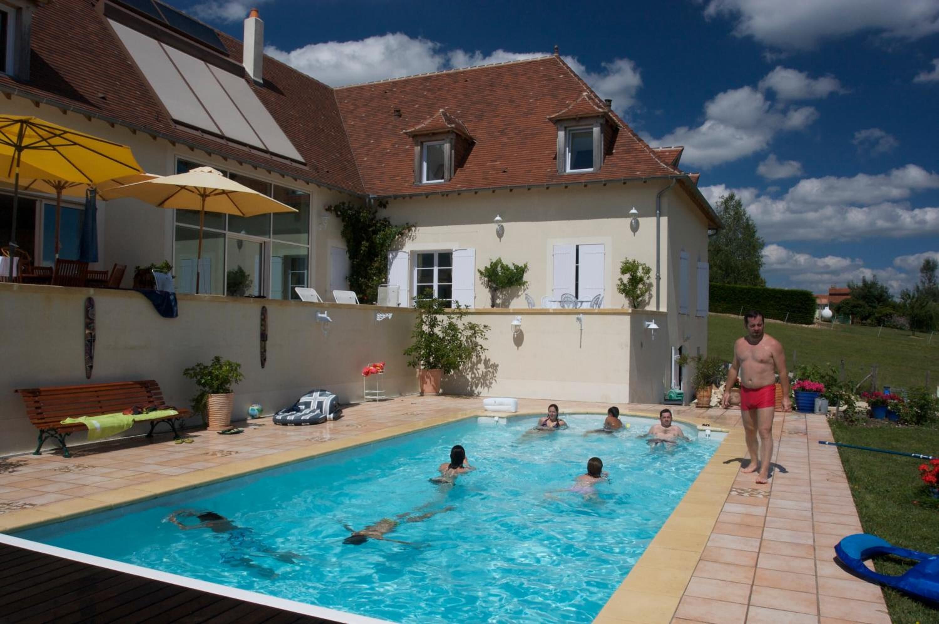 Area piscina con una casa sullo sfondo, una panchina e ombrelloni.